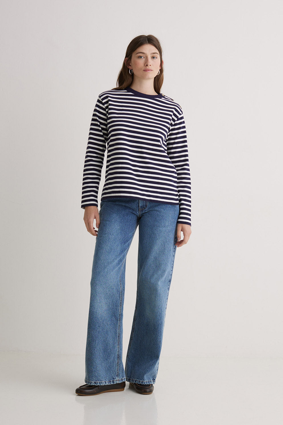 Woman wearing a navy and white striped long sleeve tee shirt  and blue jeans on a white background