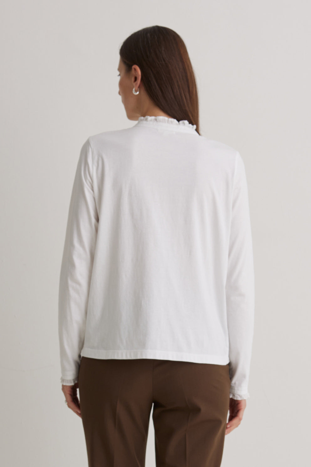 Woman wearing a white blouse and brown pants against a plain background