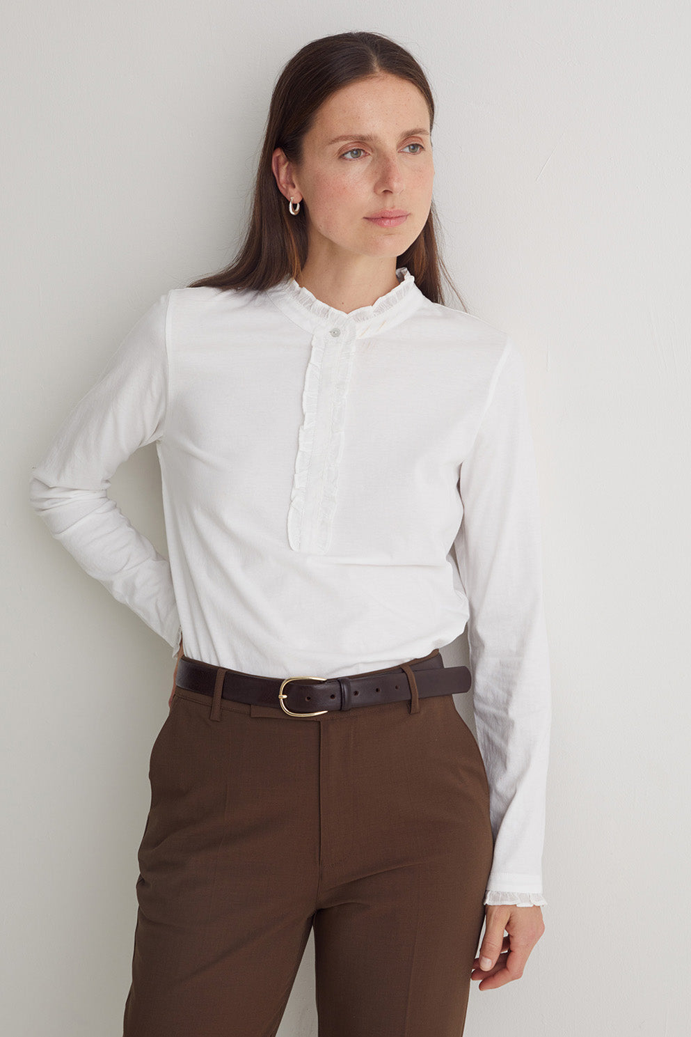 Woman wearing a white shirt and brown pants against a plain background