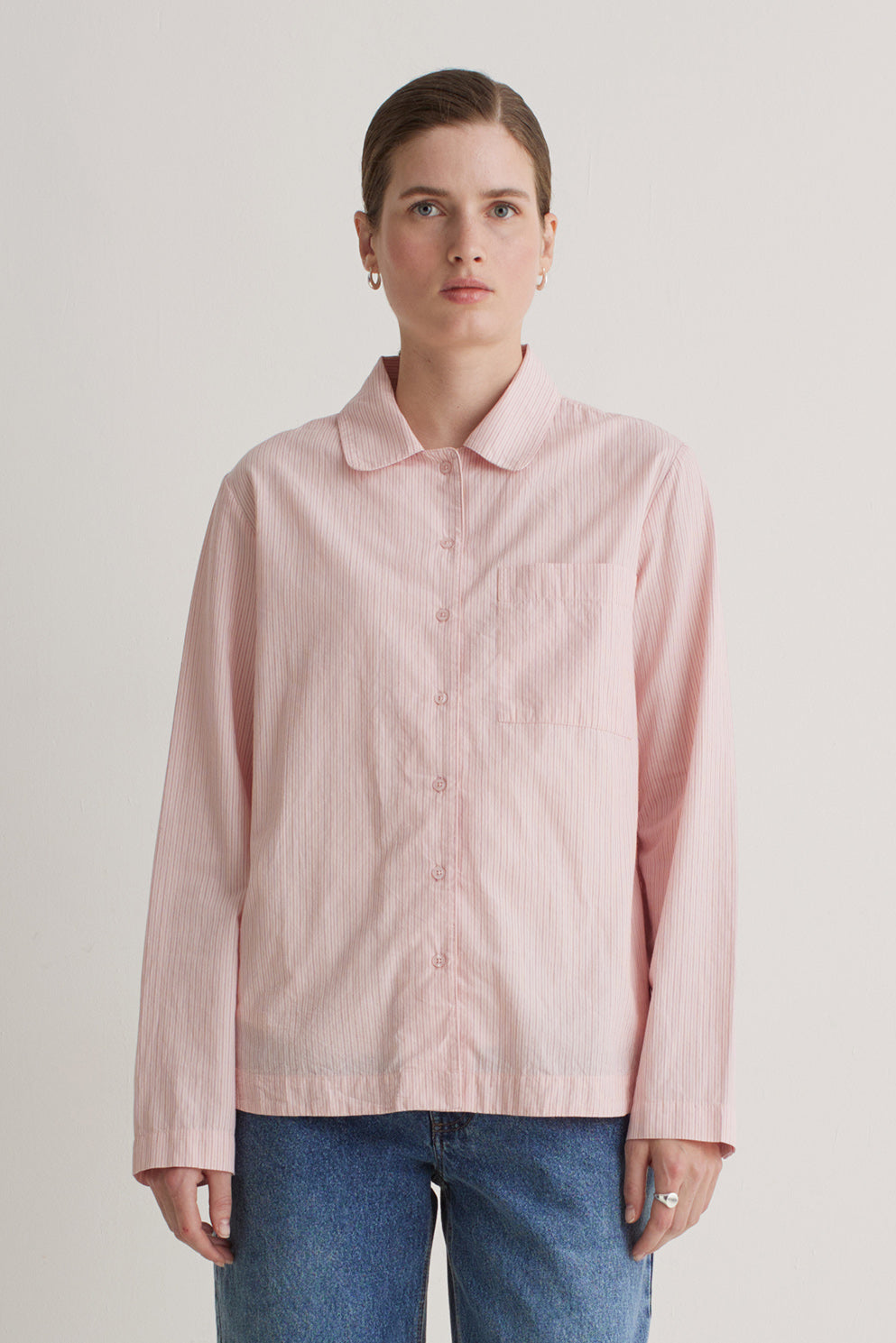 Person wearing a light pink button-up shirt and blue jeans against a plain background