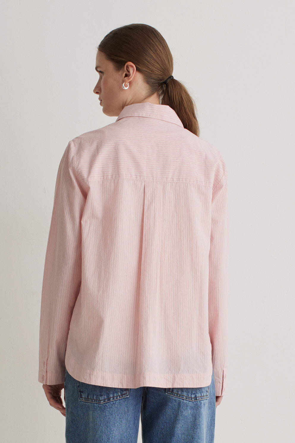 Person wearing a light pink shirt and blue jeans on a plain background