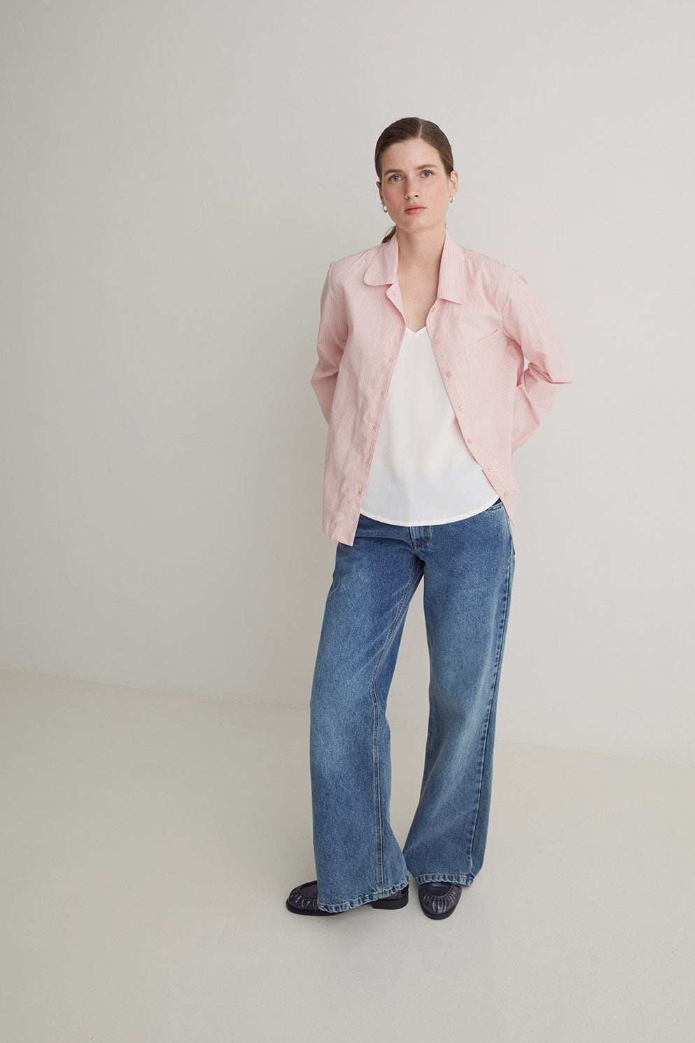 Woman wearing a pink jacket, white shirt, and blue jeans on a plain background