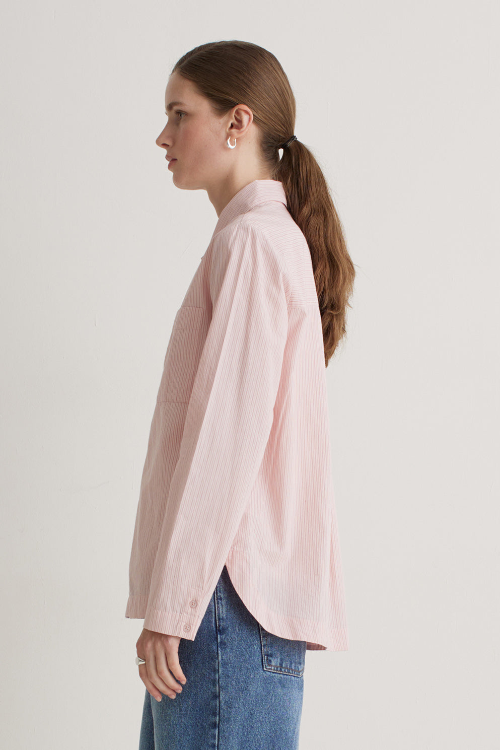 Woman wearing a light pink shirt and blue jeans on a plain background