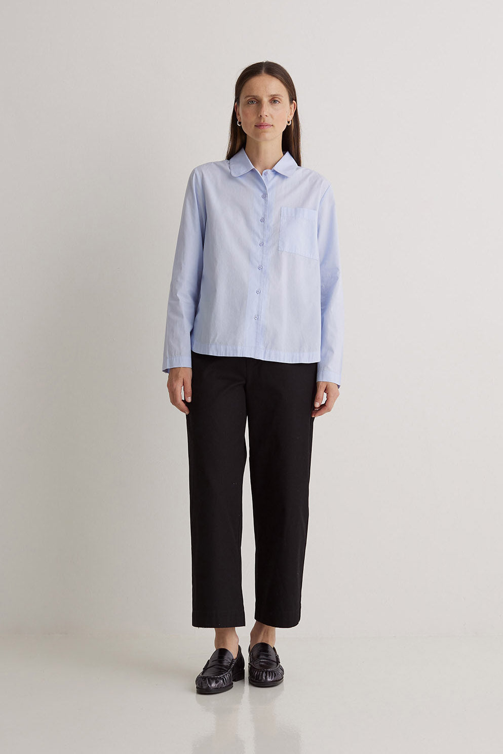 Woman wearing a light blue striped shirt and black pants on a white background