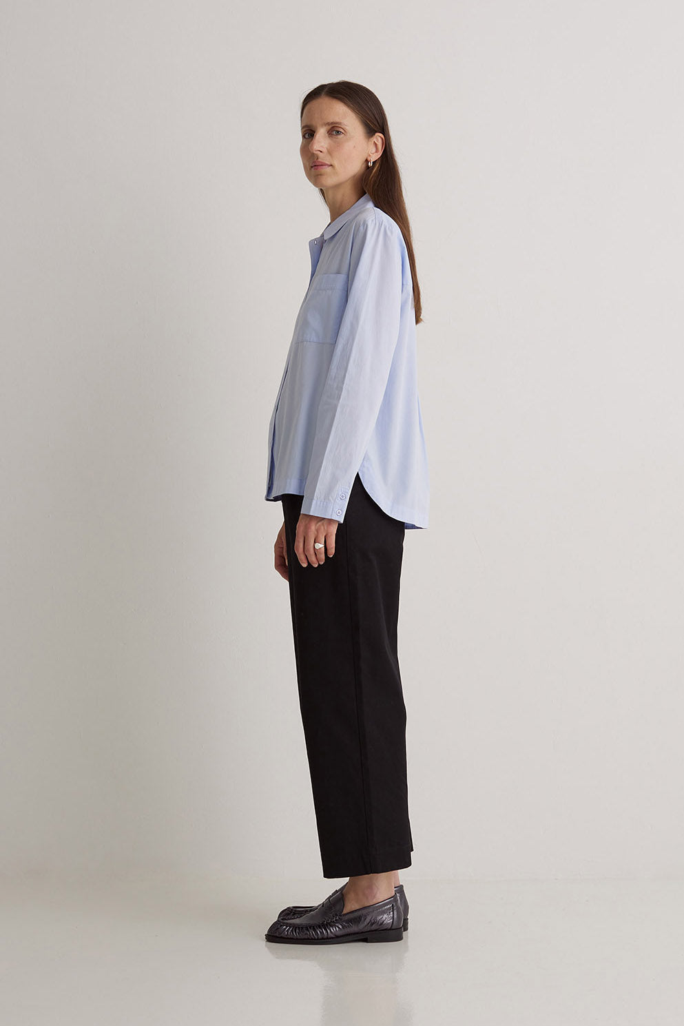 Woman wearing a light blue and white striped shirt with black pants on a white background