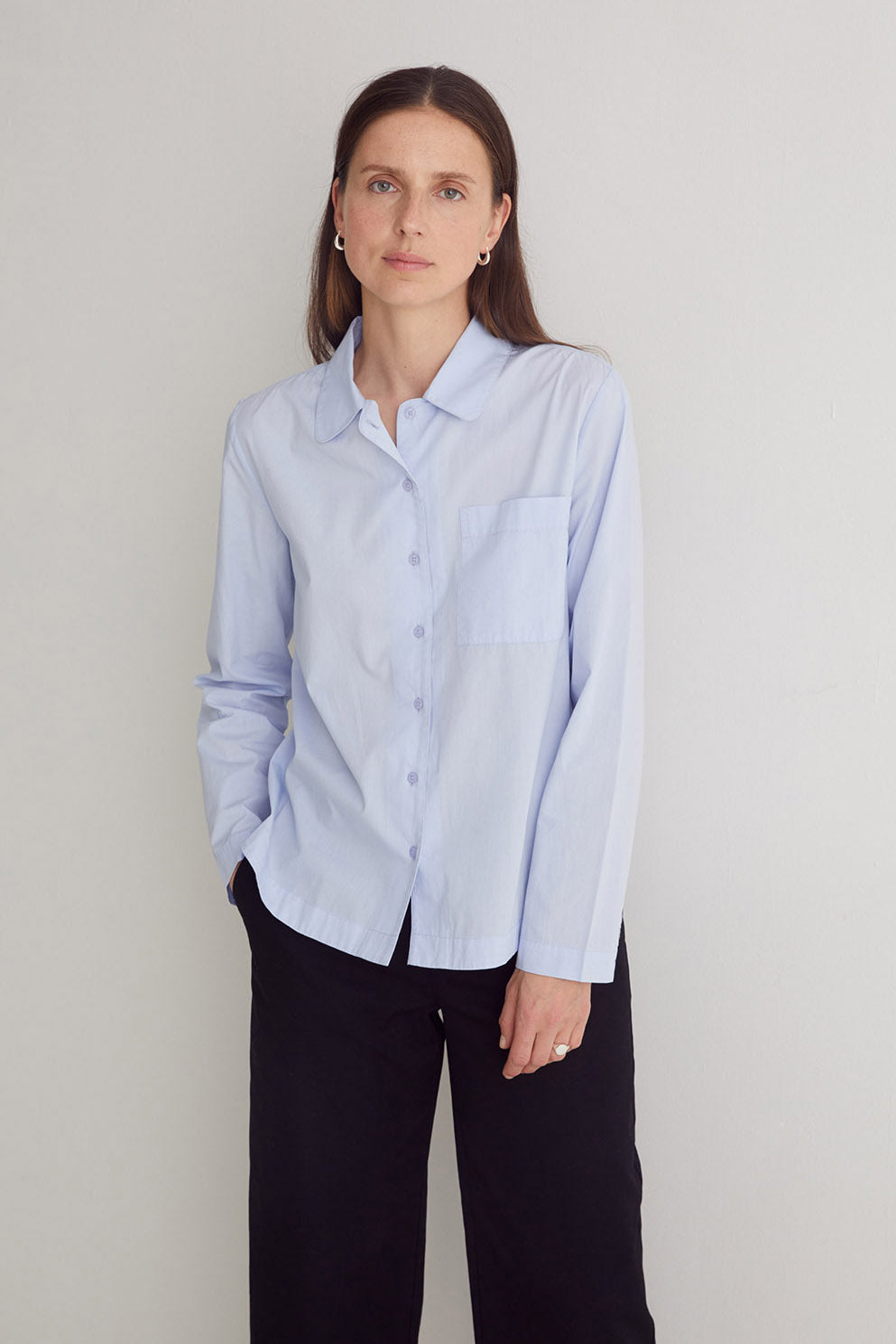 Woman wearing a light blue button-up shirt and black pants against a plain background