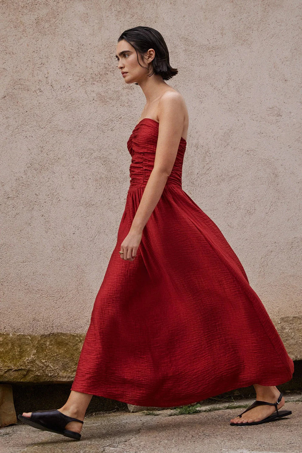 Woman wearing a red strapless dress against a textured wall.