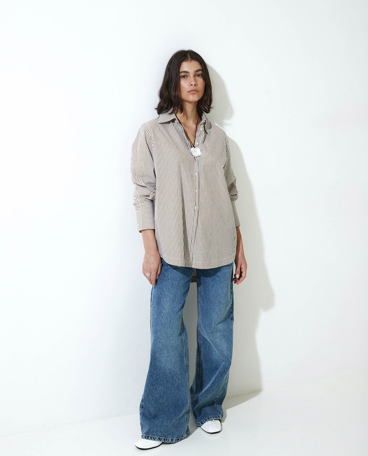Woman wearing a beige button-up shirt and blue jeans on a white background