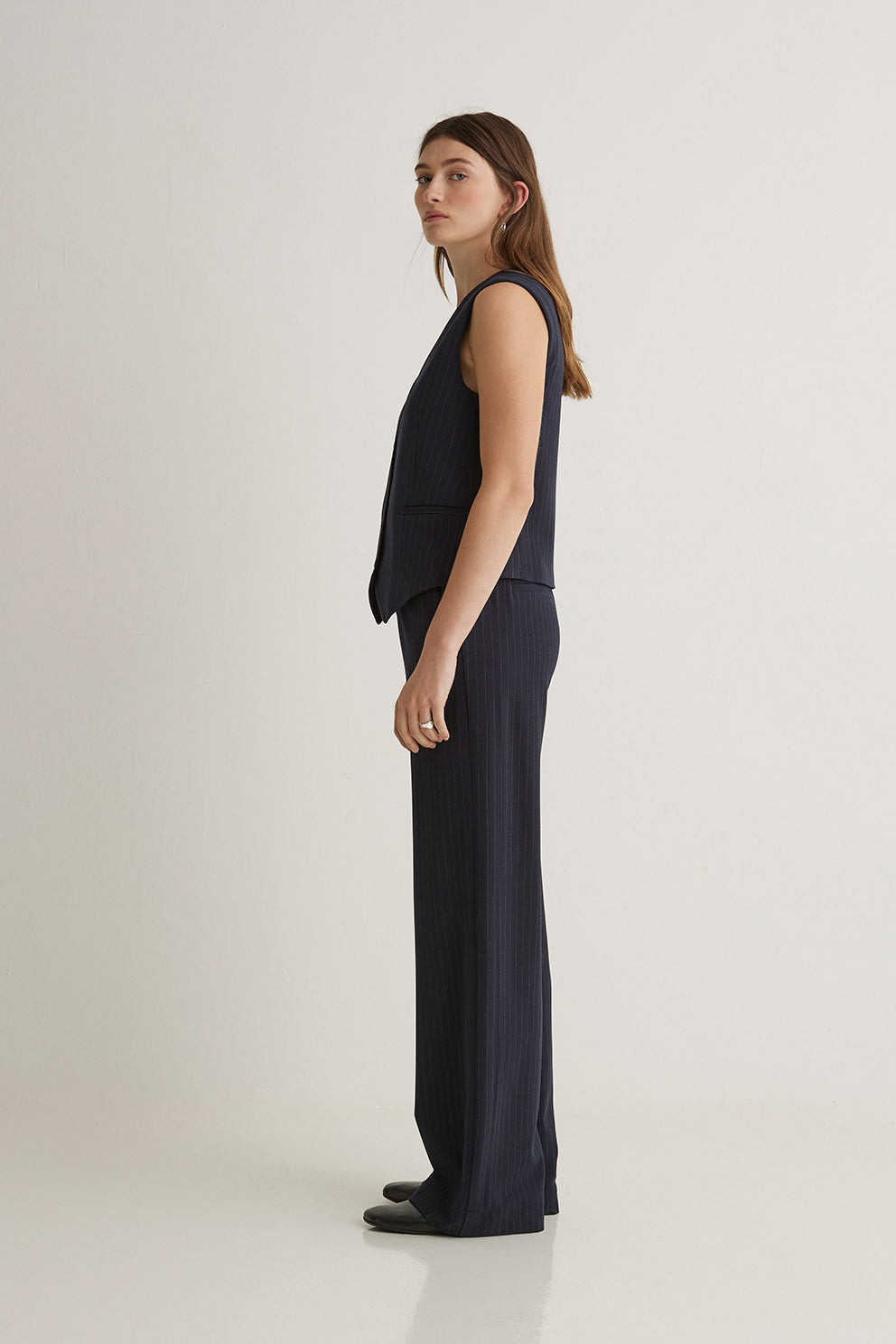 Woman wearing a sleeveless navy top and long navy pants on a white background