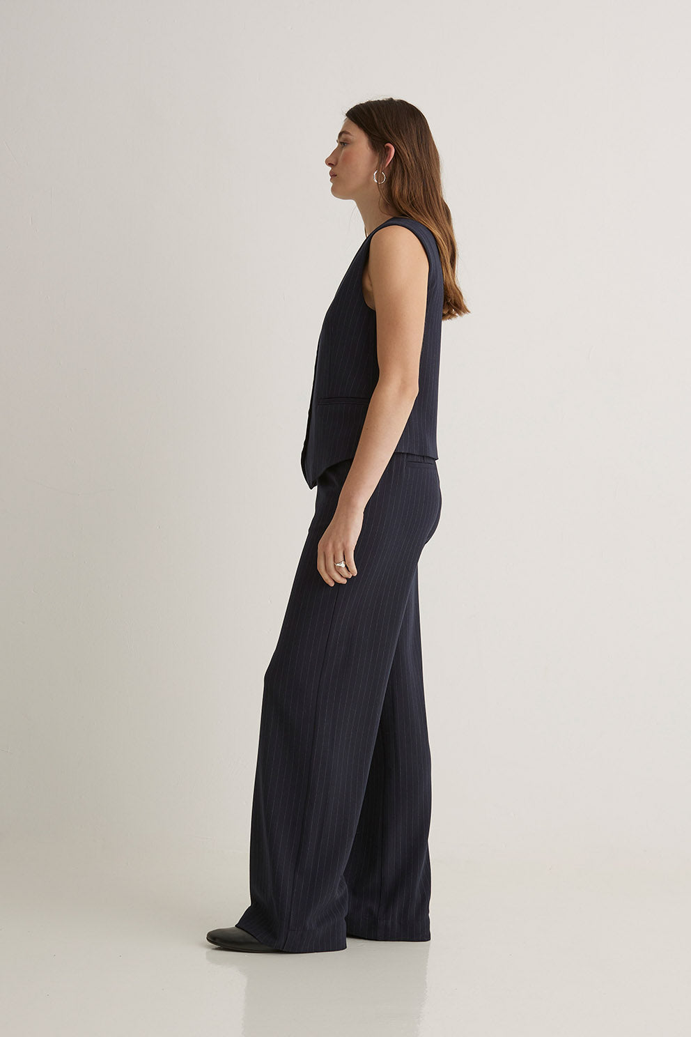 Woman wearing a dark blue sleeveless top and wide-leg pants on a white background