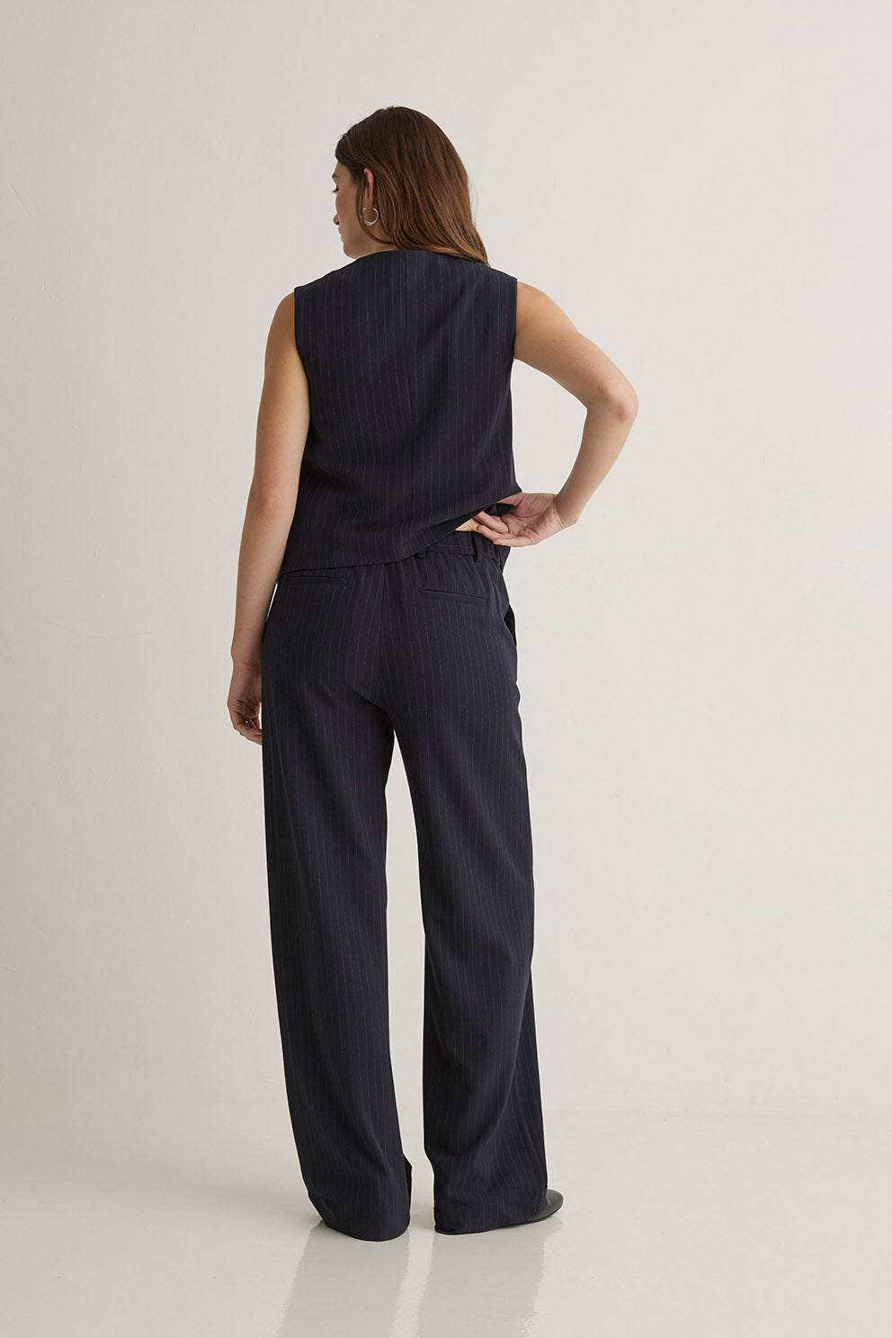 Person wearing a dark blue sleeveless top and wide-leg pants on a white background