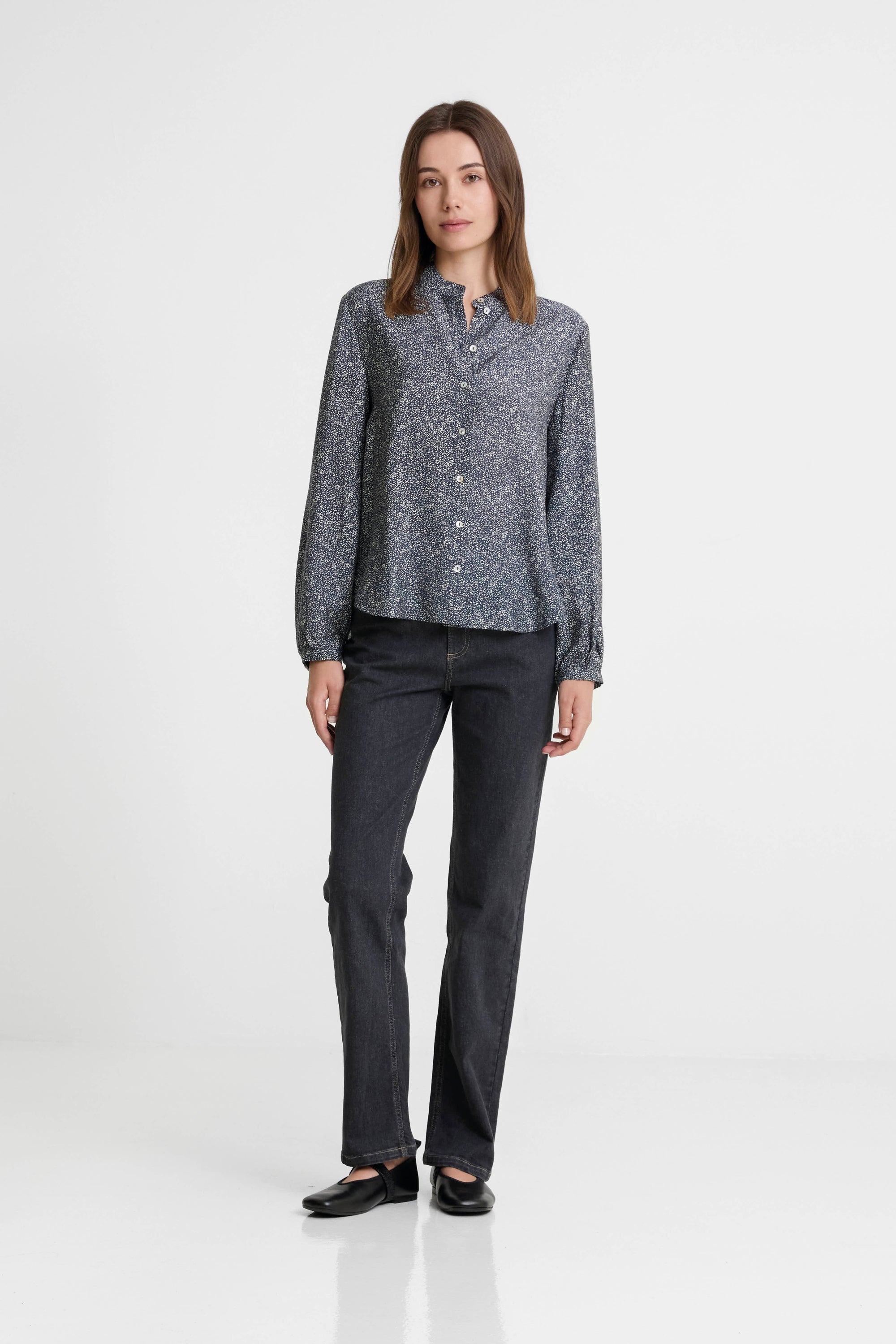 Woman wearing a patterned shirt and dark jeans on a white background