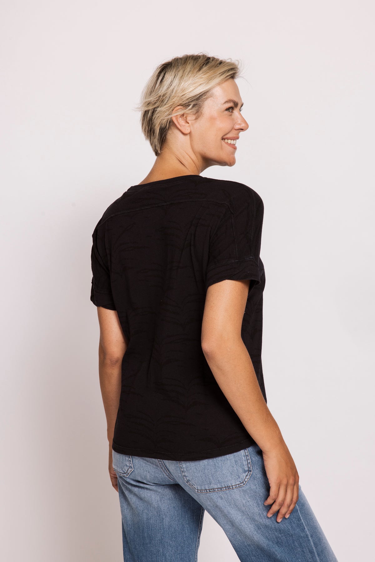 Woman wearing a black t-shirt and blue jeans against a plain background