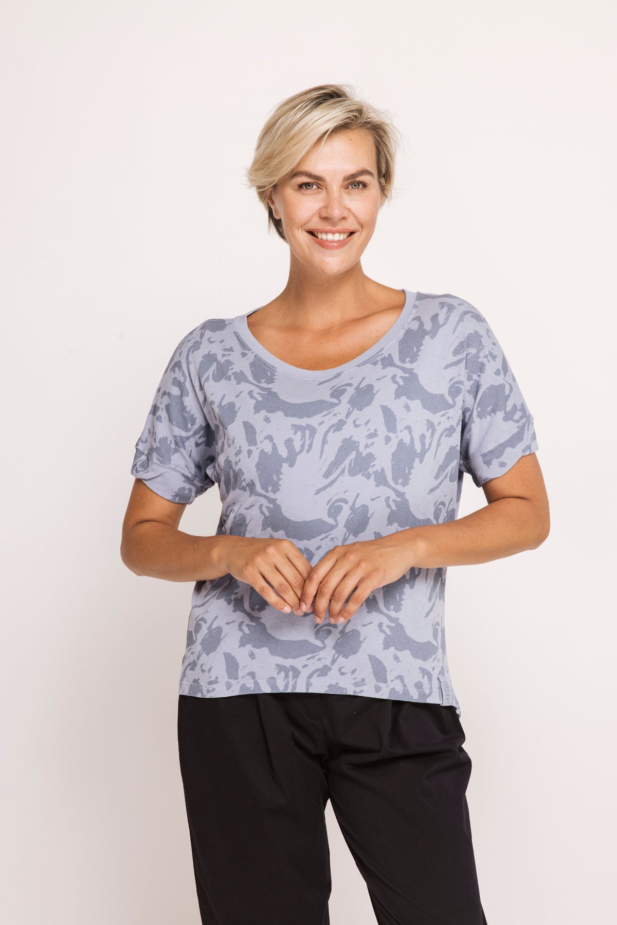 Woman wearing a patterned shirt and black pants on a white background