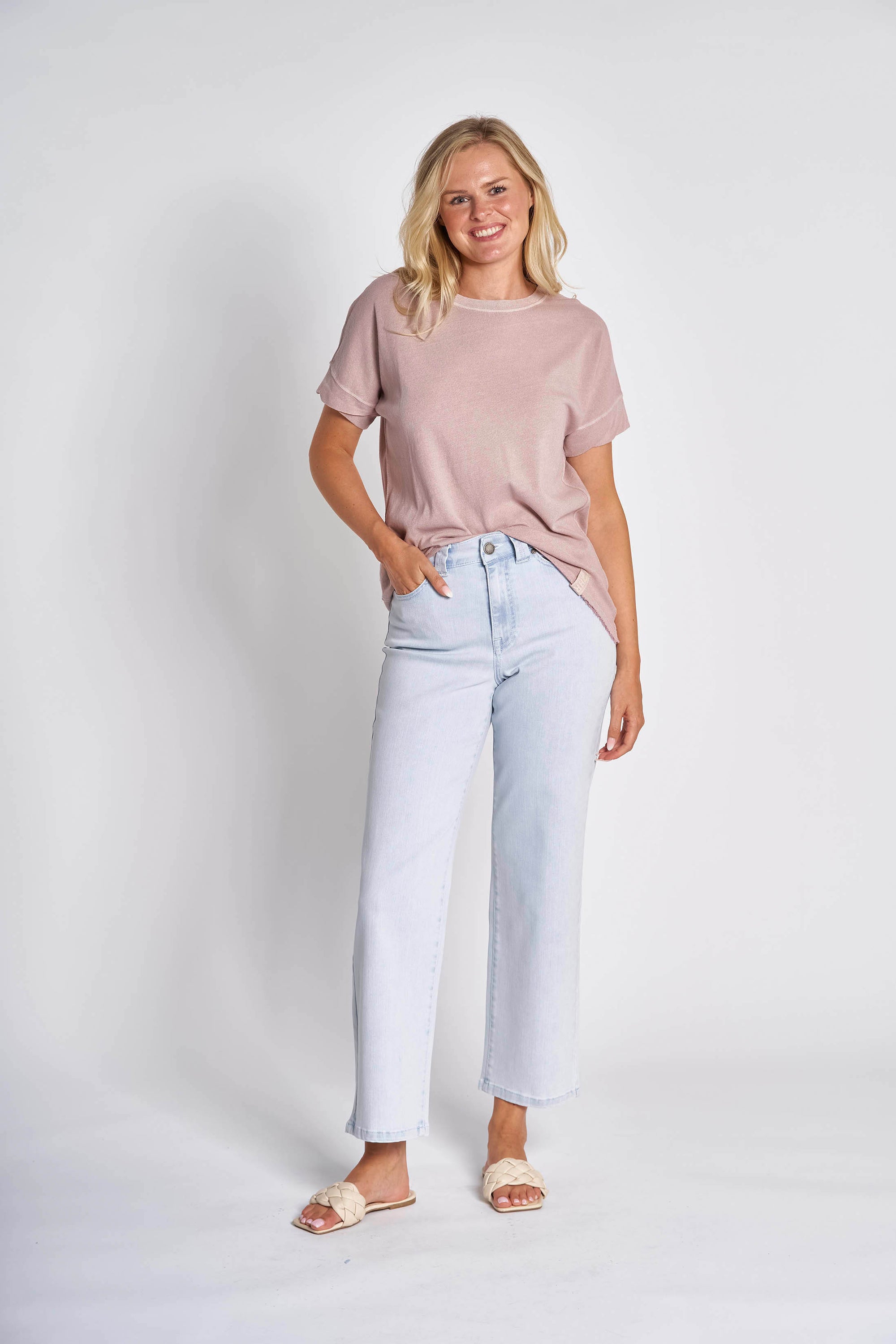 Model wearing light lavender (pink) t shirt with round neck and light coloured jeans on white background.