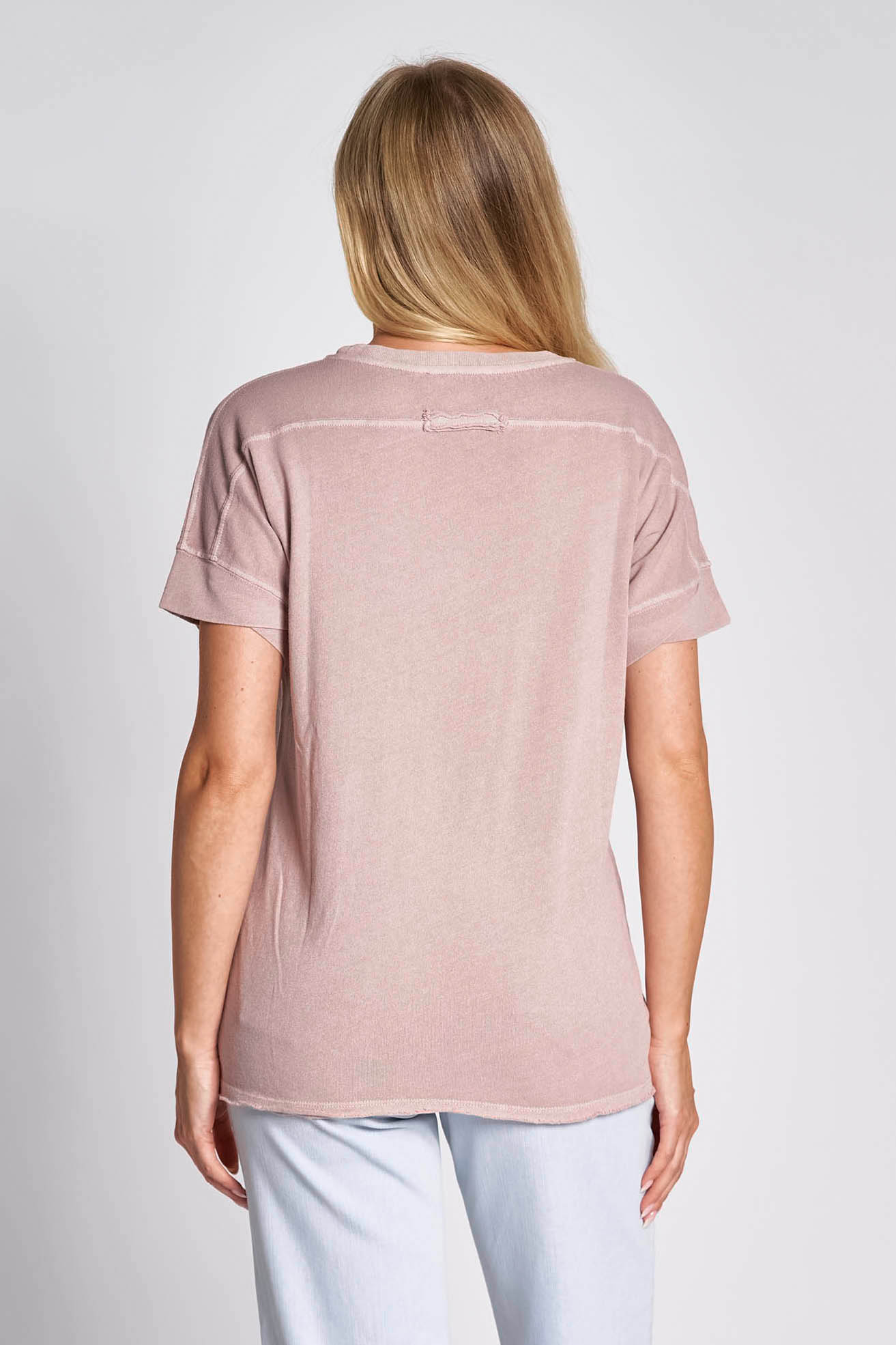 Model wearing light lavender (pink) t shirt with round neck and light coloured jeans on white background.