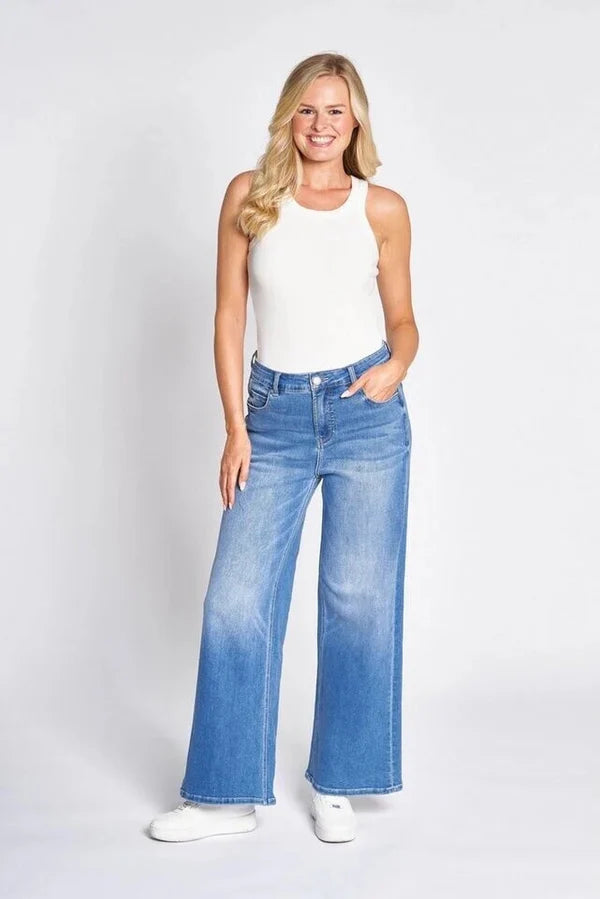 Blue wide leg denim jeans on model with white tank top and sneakers on white background 