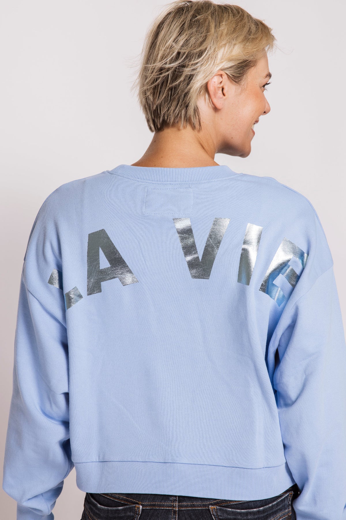 Person wearing a light blue sweatshirt with 'Lavie' printed on the back against a plain background