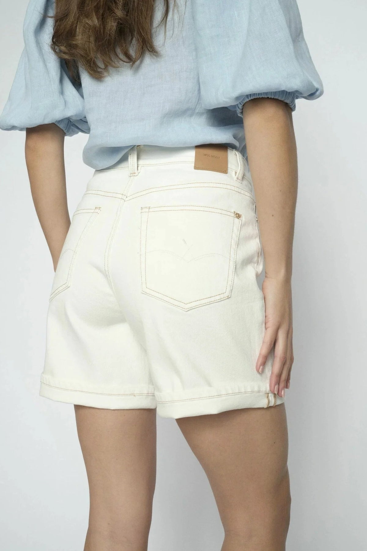 A person shown from the back wearing off-white denim shorts and a light blue puff-sleeve blouse against a plain light gray background.