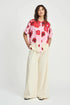 Woman wearing a pink floral blouse and beige wide-leg pants on a white background