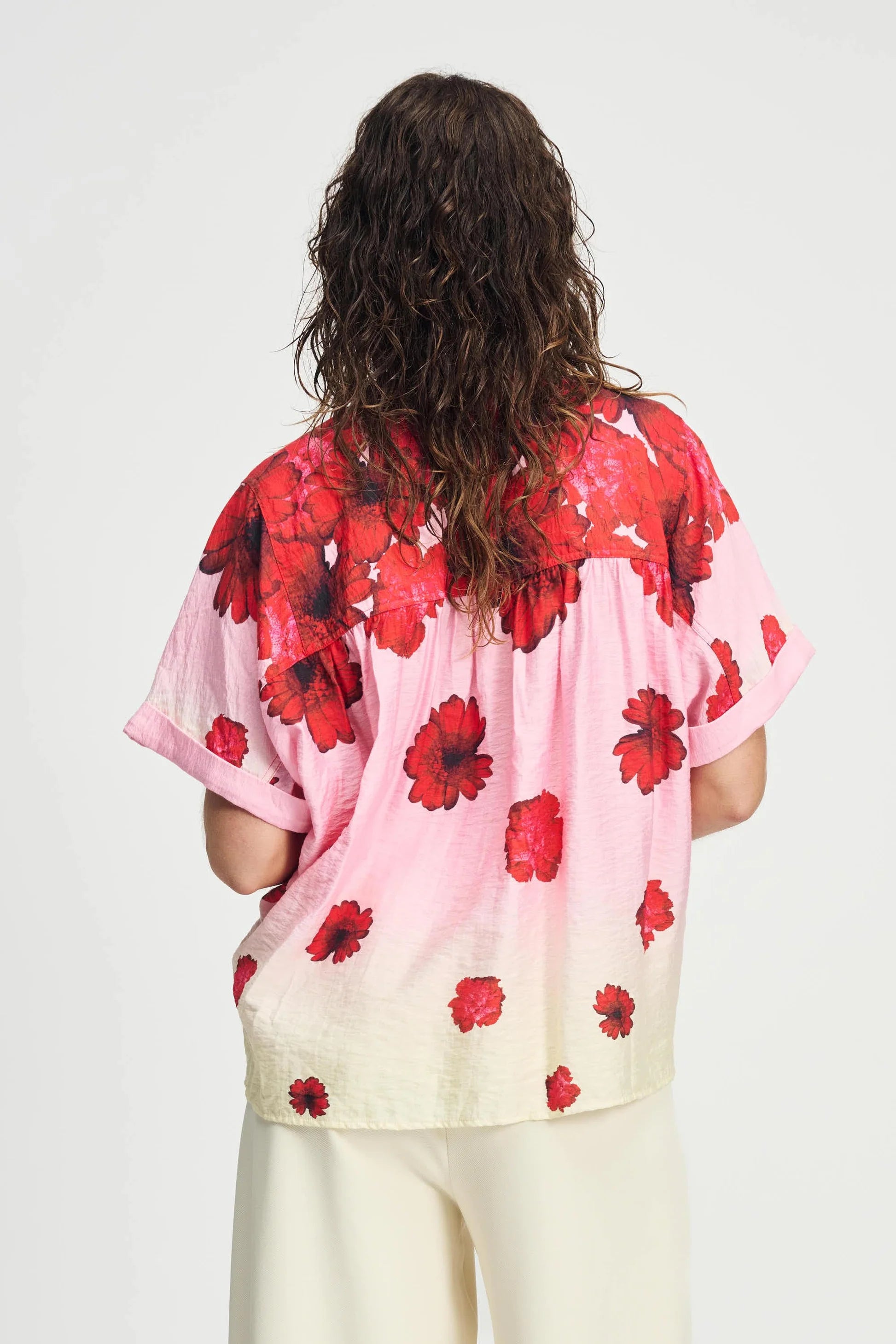 Woman wearing a pink floral short sleeve blouse and cream pants on a white background 