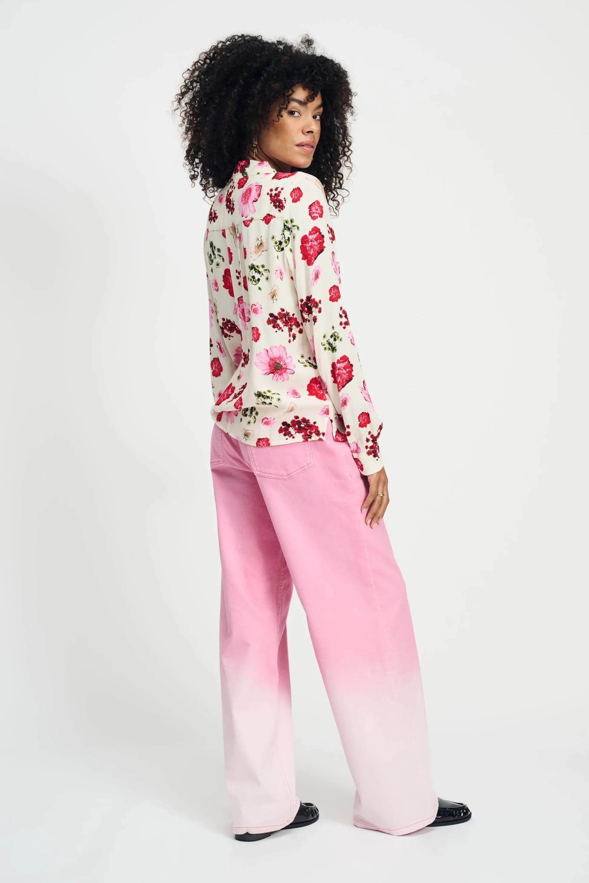 Woman wearing a long sleeve floral blouse and pink pants against a white background
