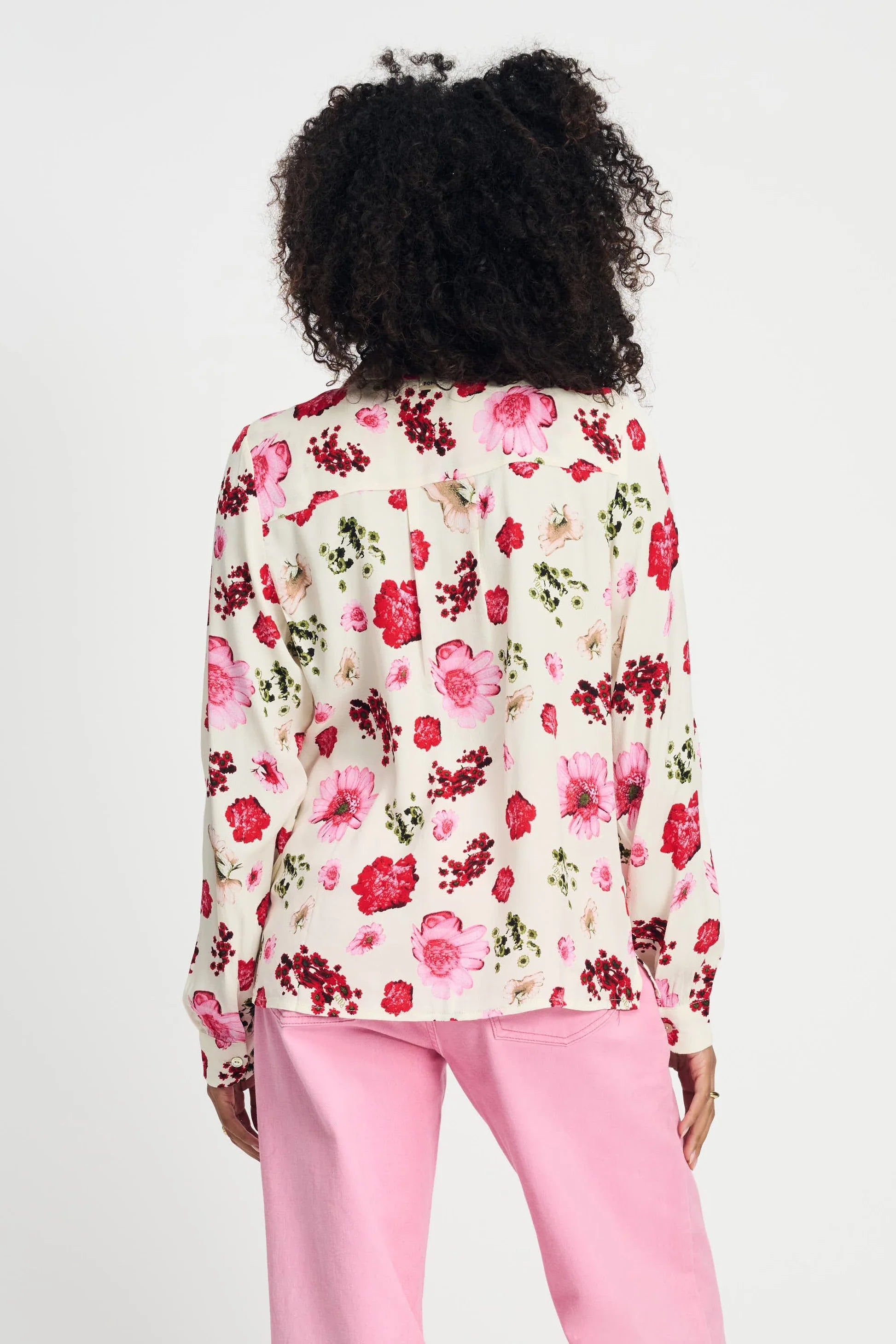 Woman wearing a long sleeve floral blouse and pink pants against a white background
