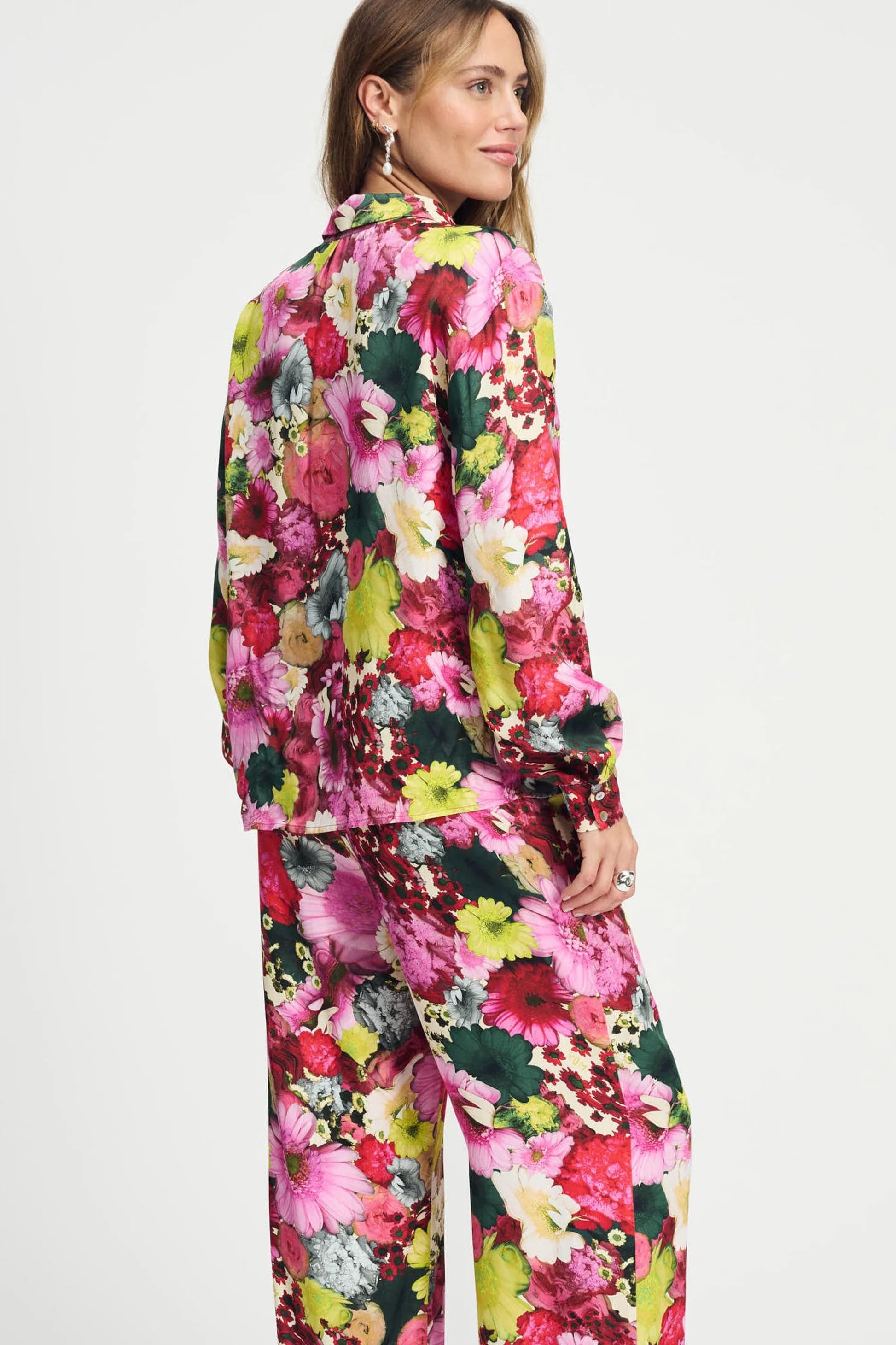 Model wearing a long sleeve bright floral blouse and matching pant on a plain background