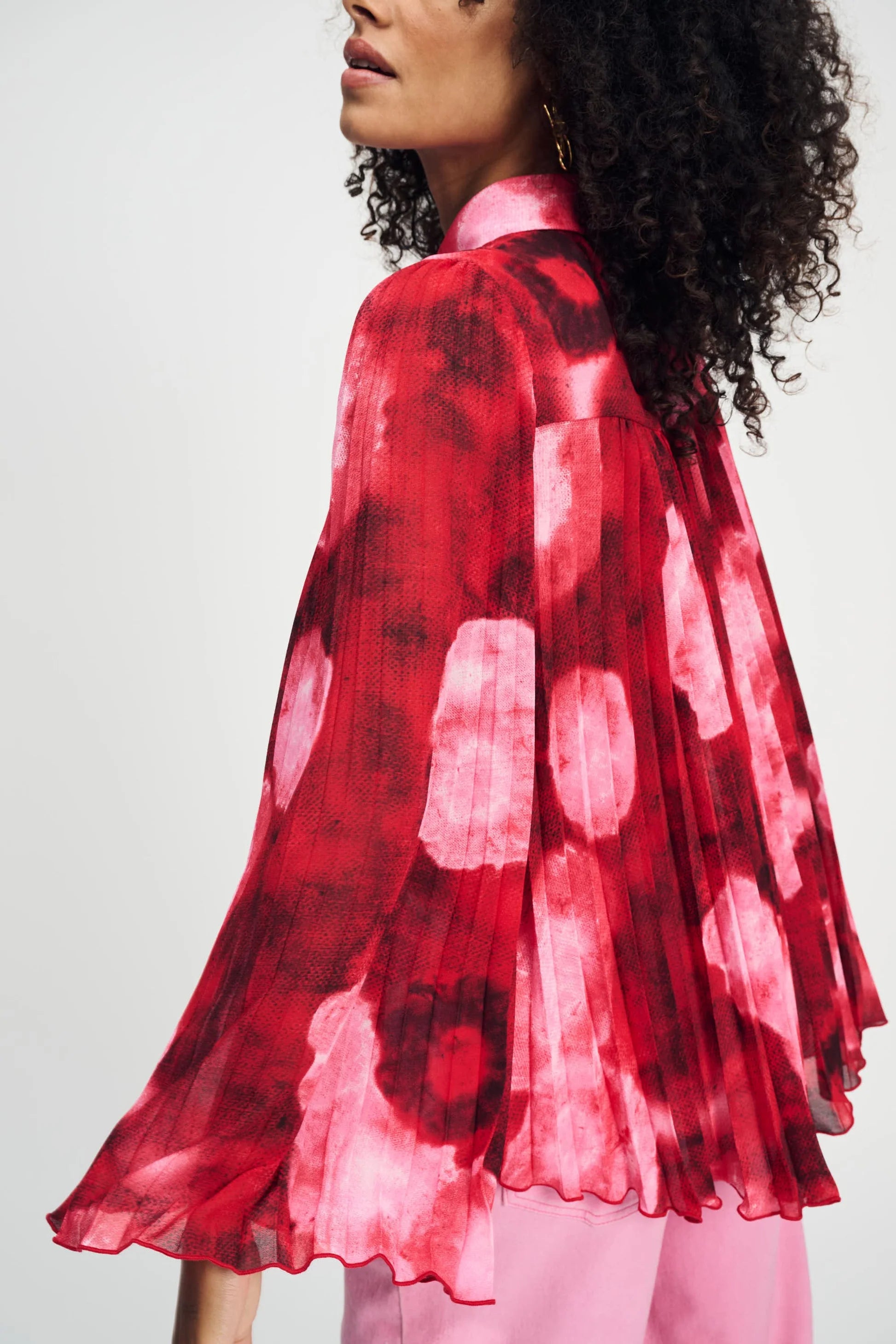 Model wearing long sleeve red and pink floral shirt with wide sleeves and pink pants on a plain background. 