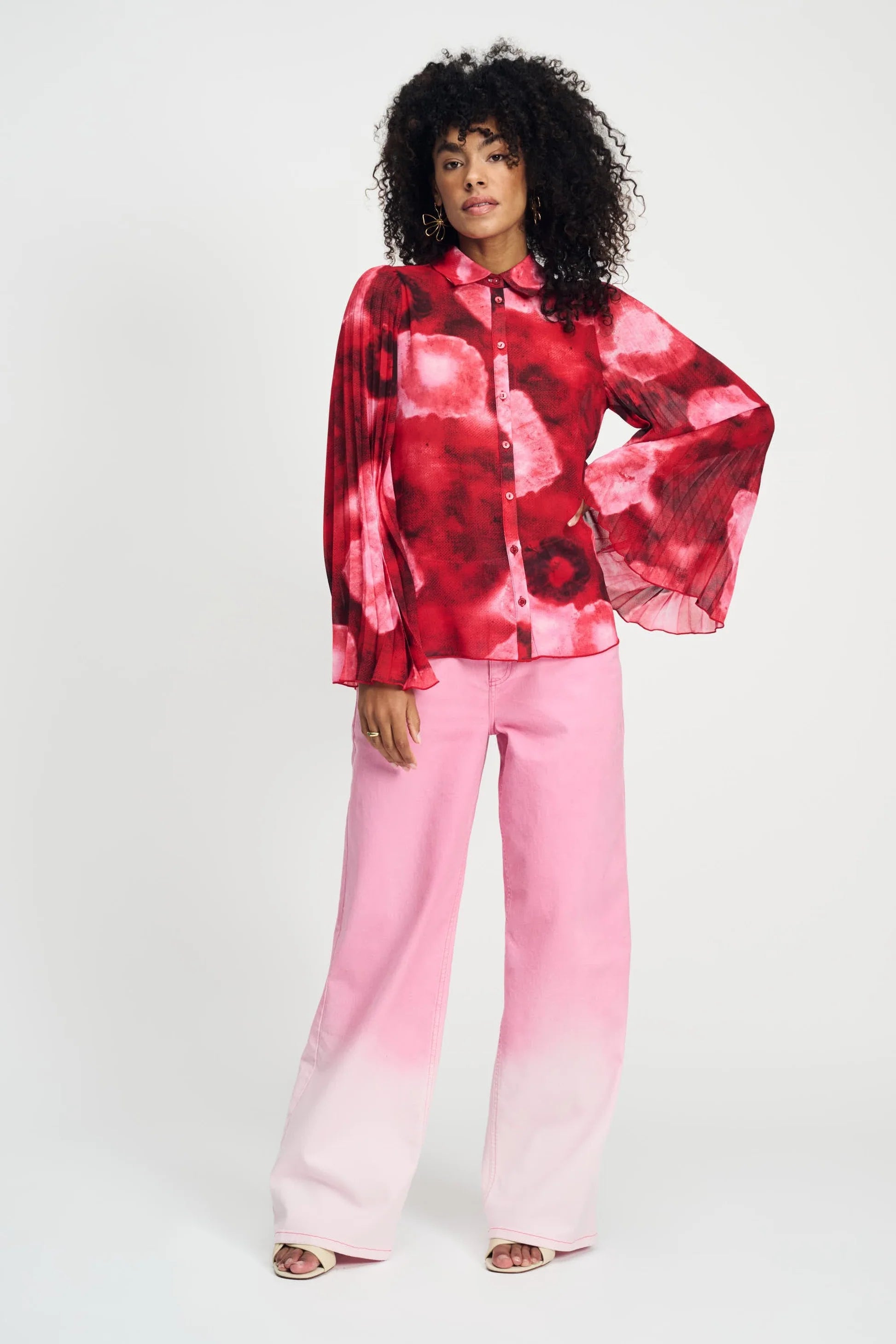 Model wearing long sleeve red and pink floral shirt with wide sleeves and pink pants on a plain background. 