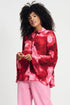 Model wearing long sleeve red and pink floral shirt with wide sleeves and pink pants on a plain background. 