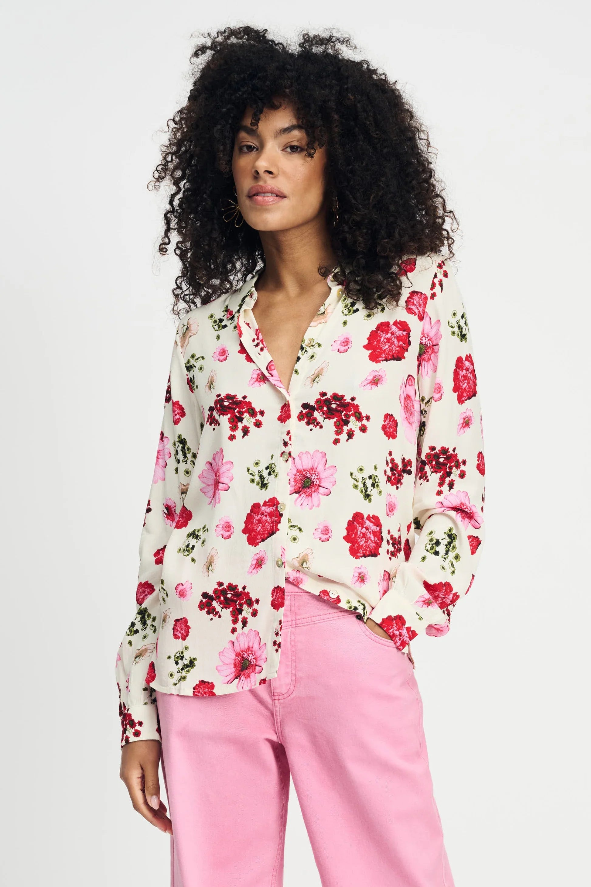 Woman wearing a long sleeve floral blouse and pink pants against a white background