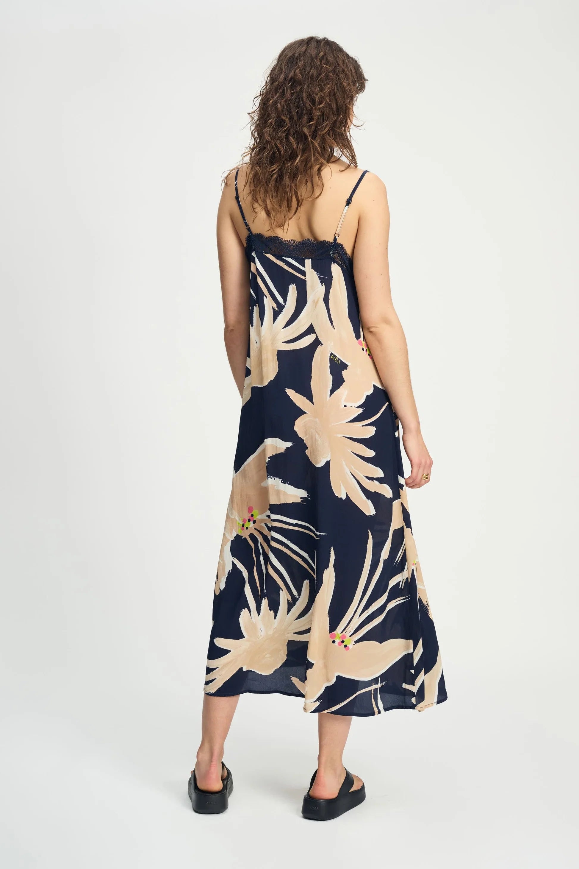Woman wearing a navy cami dress with beige floral pattern on a white background