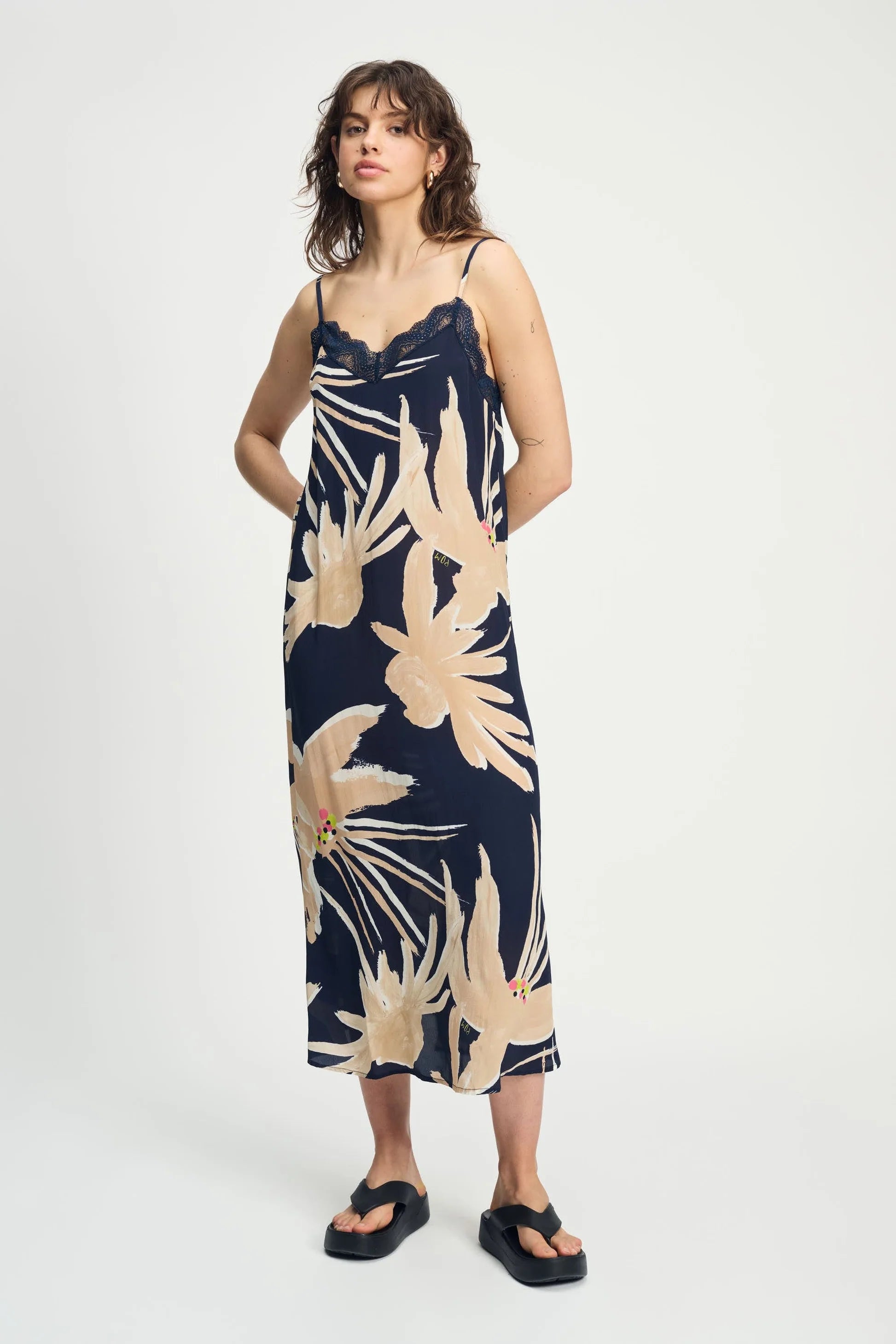 Woman wearing a navy cami dress with beige floral pattern on a white background