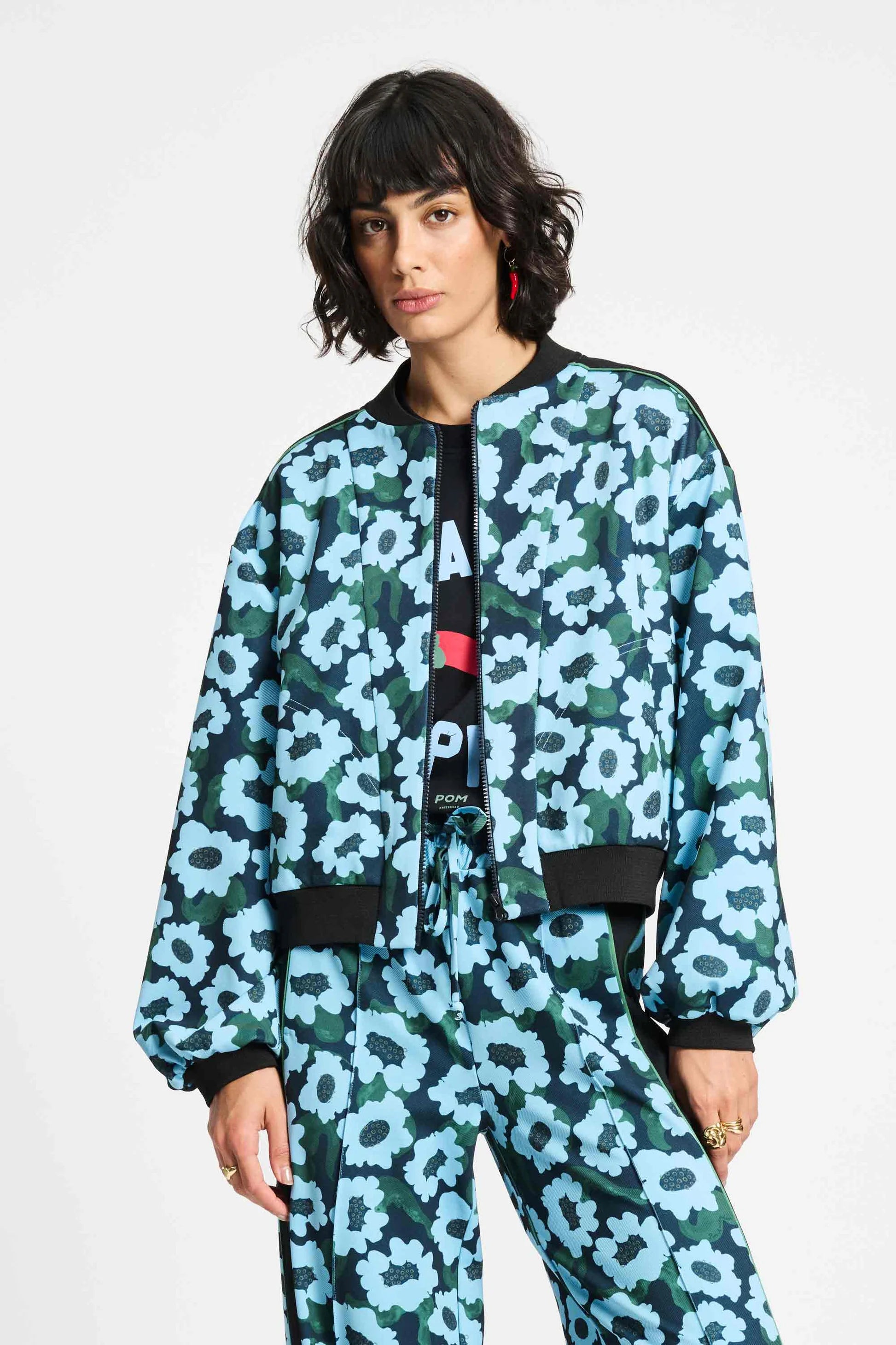 Woman wearing a blue and green floral bomber jacket and matching pants on a white background