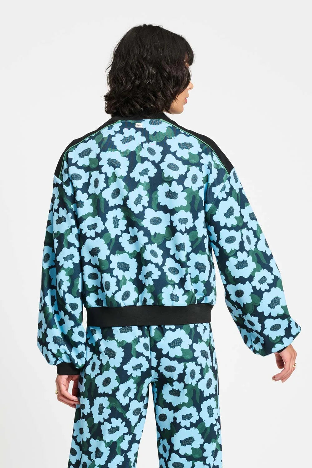 Woman wearing a blue and green floral bomber jacket and matching pants on a white background