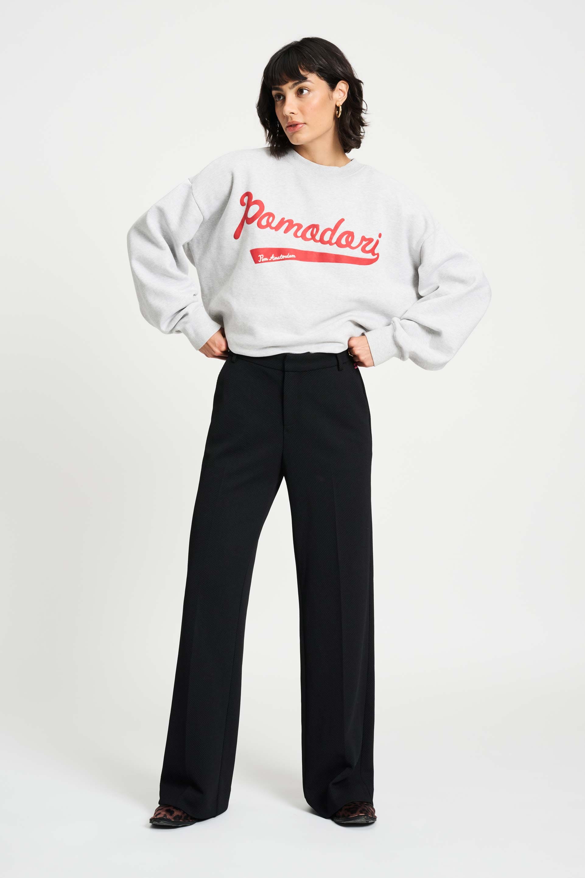 Woman wearing a grey sweatshirt with red text and black pants on a white background