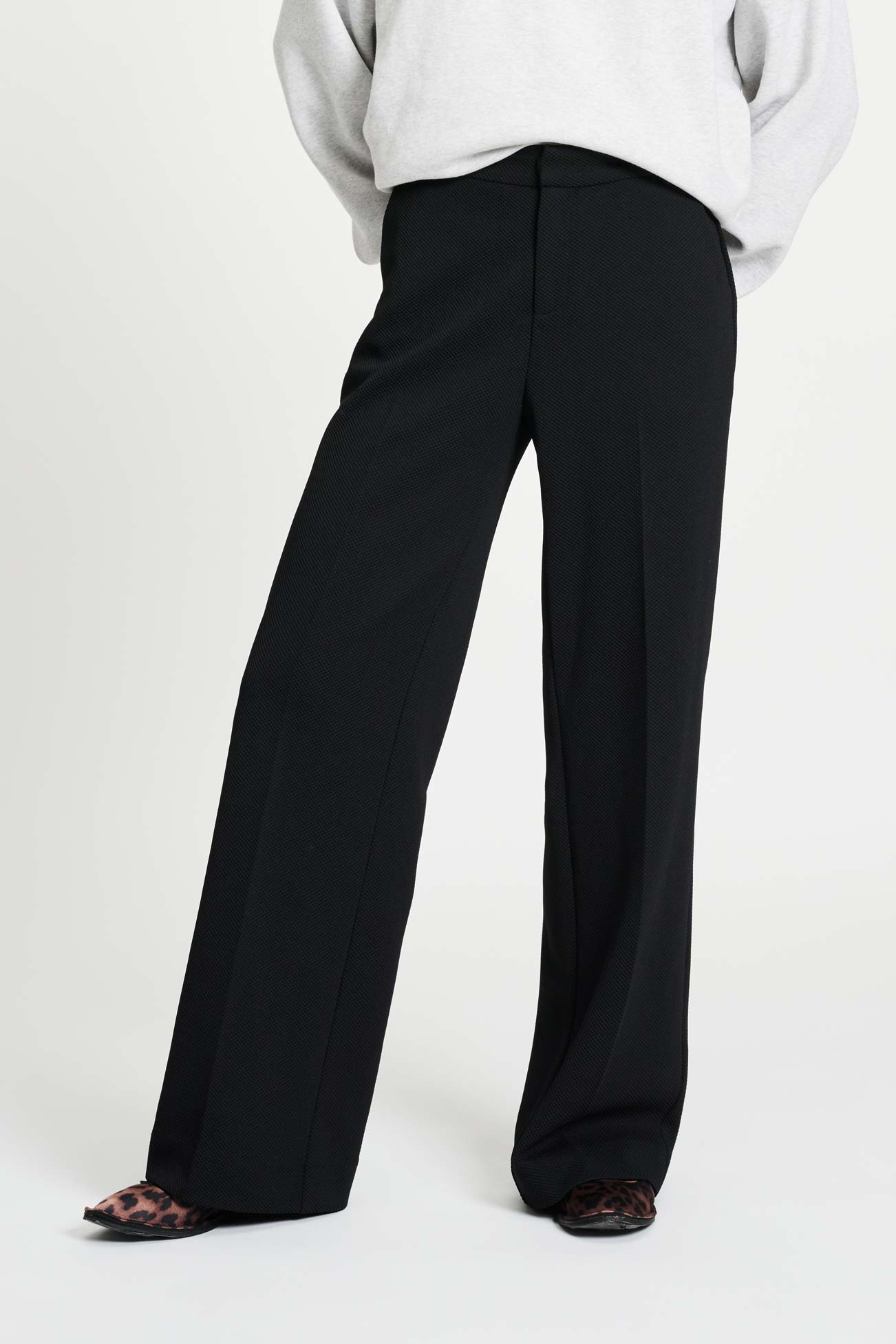 Woman wearing black wide-leg pants and a light grey sweater on a white background