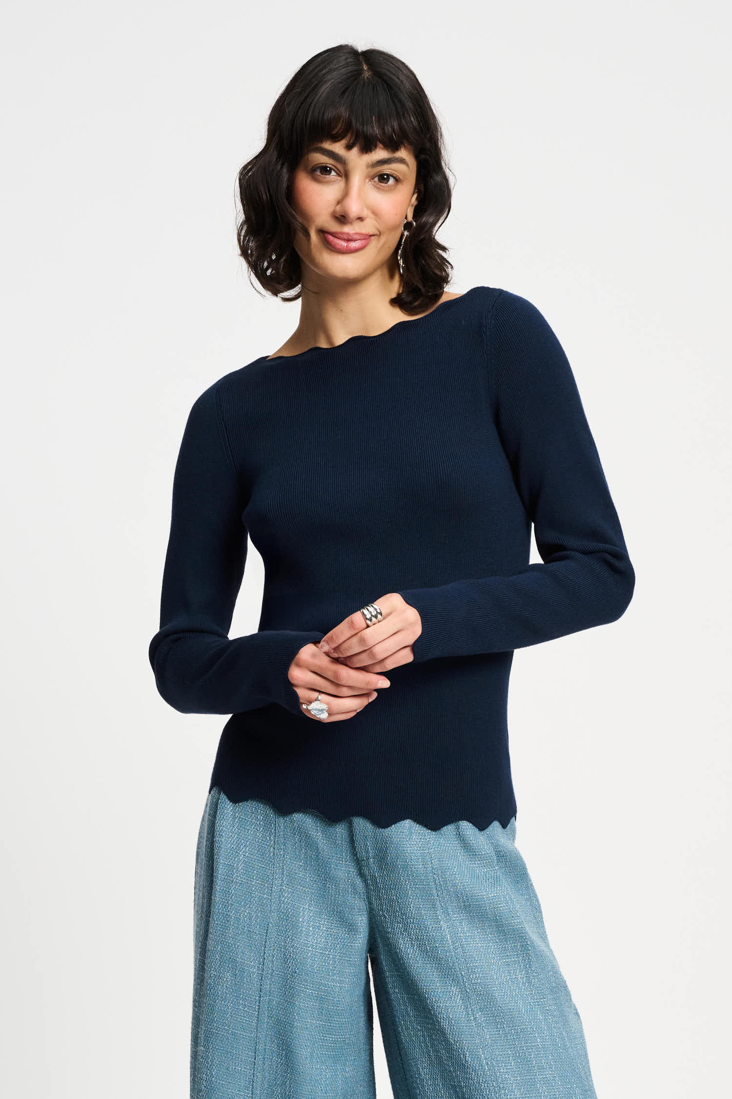 Woman wearing a navy sweater and light blue pants on a white background