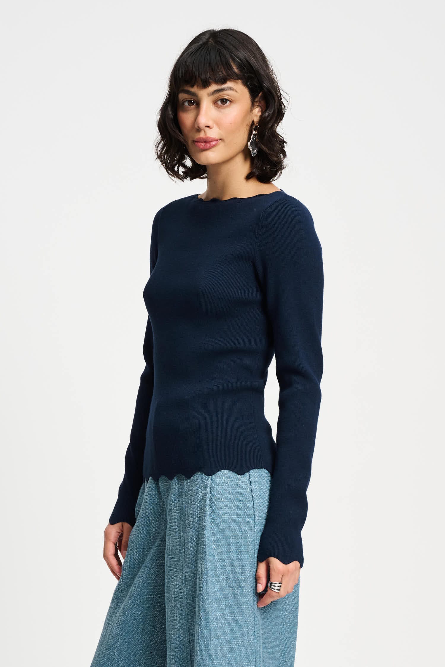 Woman wearing a navy sweater and light blue skirt on a white background