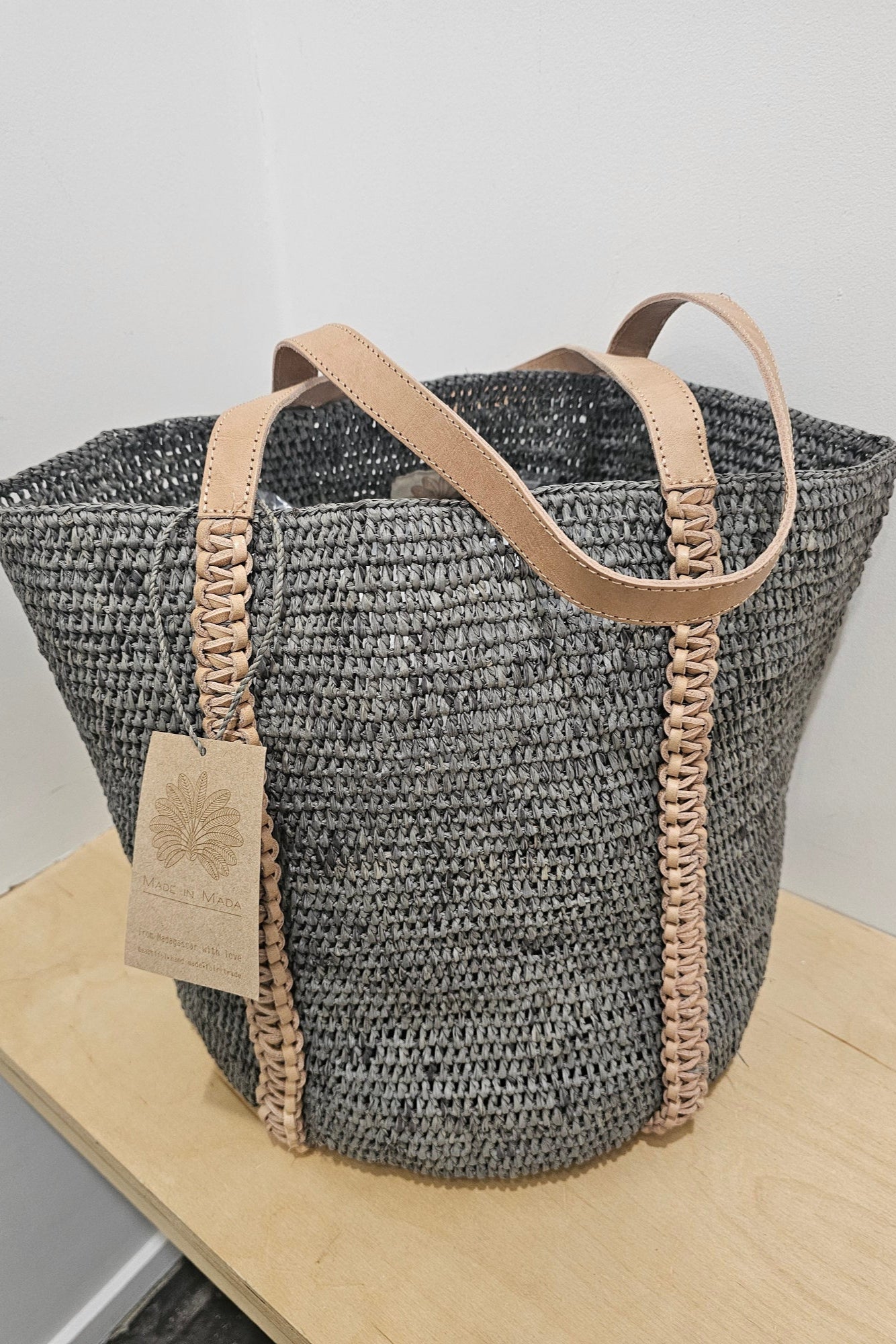 Woven handbag with brown leather trim on a white background
