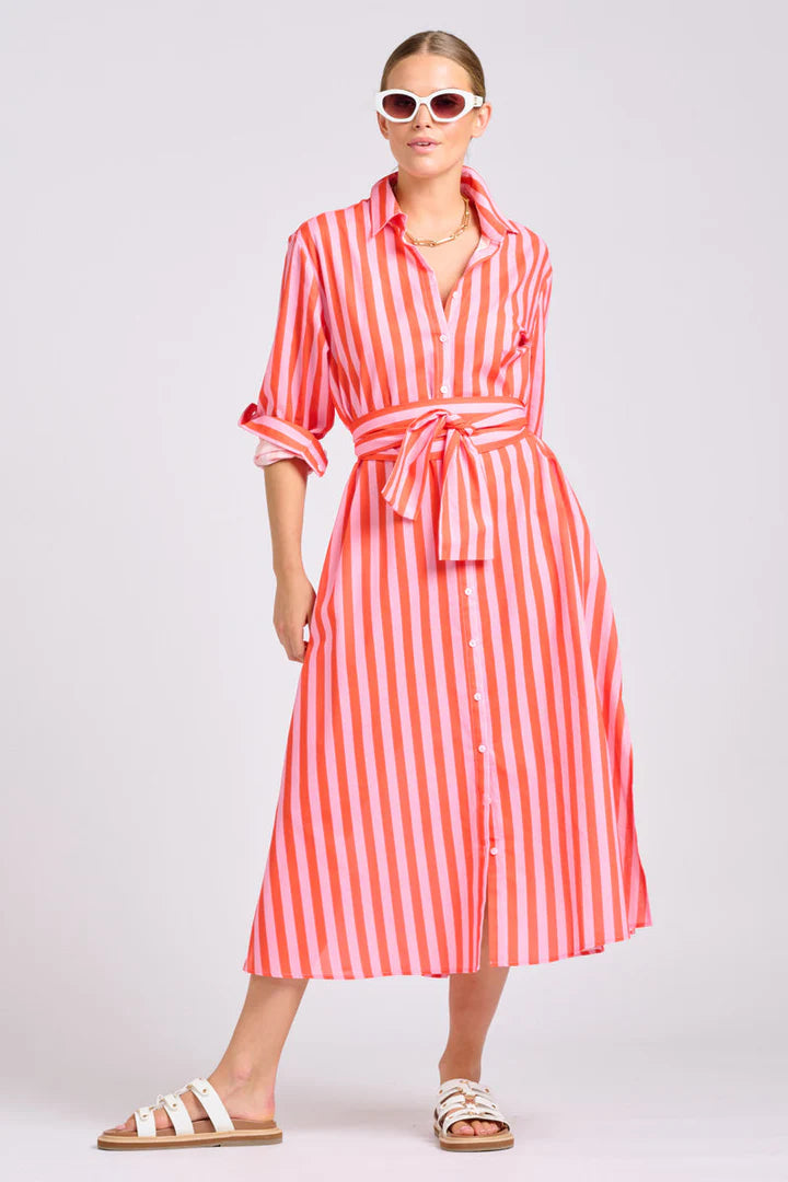 Woman wearing a papaya and light pink striped maxi shirt dress on a plain background