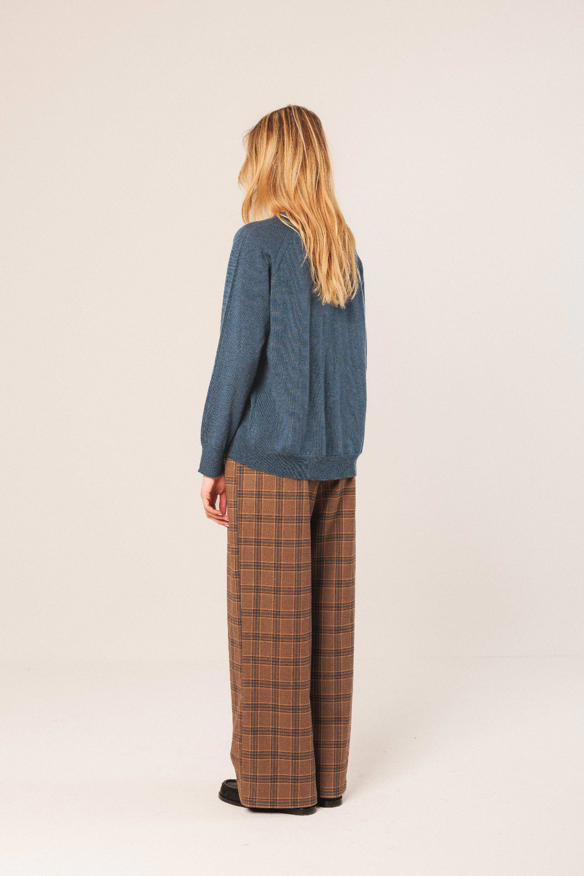 Person wearing a blue sweater and plaid pants on a white background